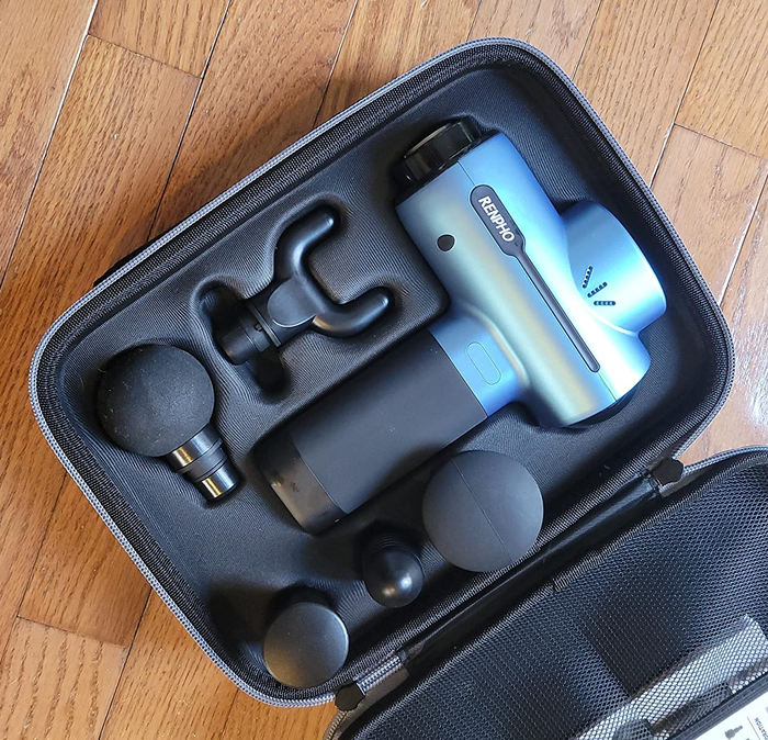 reviewer image showing the blue massage gun in its travel case along with the included massage heads