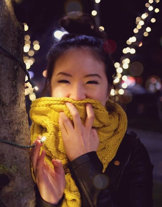Reviewer wearing a yellow scarf next to a holiday-decorated tree with lights