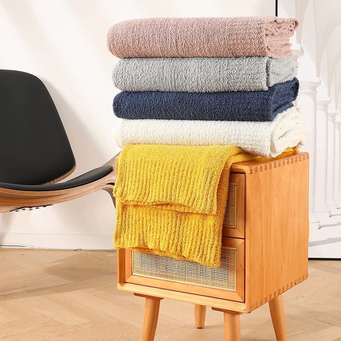 a collection of throw blankets in various colors stacked neatly on an end table