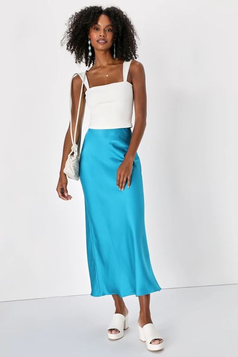A model dressed in a blue skirt, white top, and accessories.