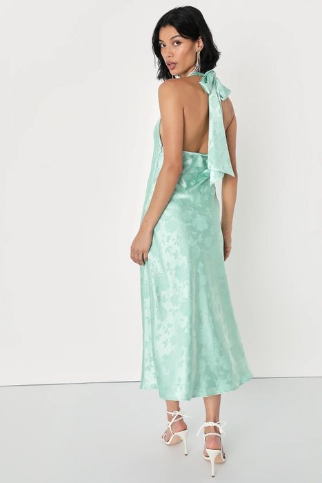 A model showcasing the back of a green dress paired with white shoes.