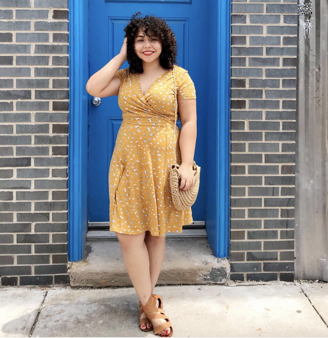 A reviewer wearing a yellow floral mini dress