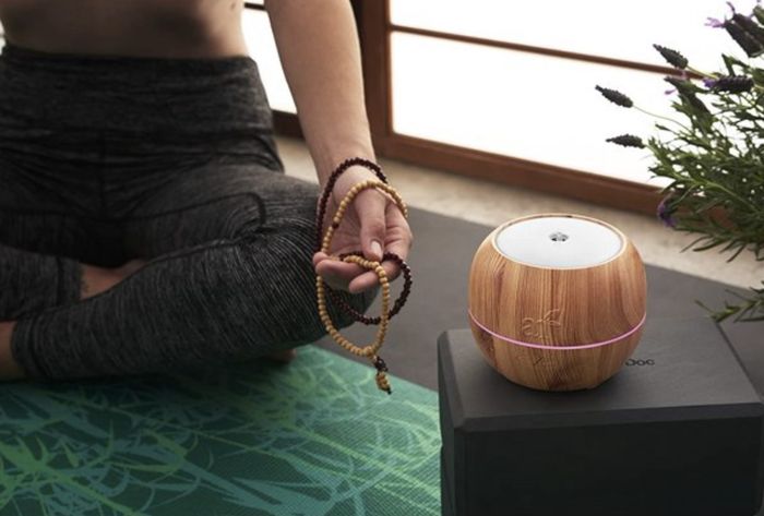 The brown wood diffuser placed on a yoga block beside someone meditating