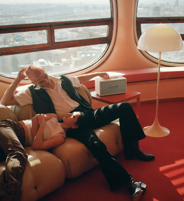 A couple lounging on a sofa next to a speaker.
