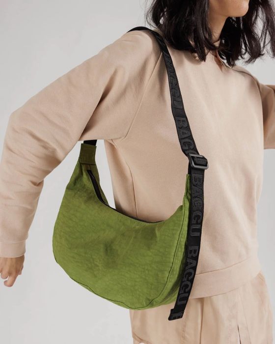 a model wearing a green crescent-shaped crossbody bag with an adjustable black nylon strap