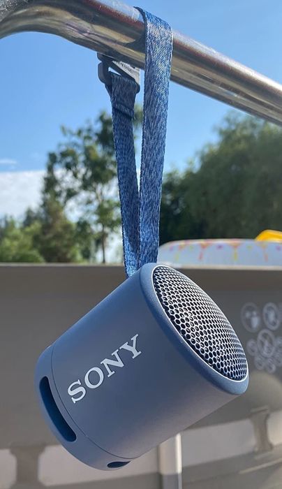 A reviewer's photo of the compact blue speaker with a fabric strap.