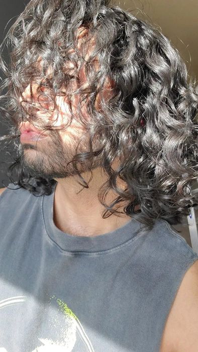 Reviewer wearing a gray tank top, showing off their shiny black curls after using the product.