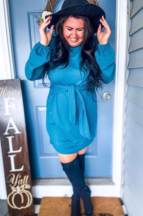 a reviewer wearing a wide-brimmed hat and the long-sleeve dress with a tie-waist detail in blue