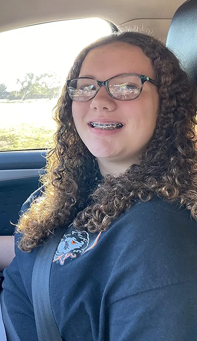 Reviewer sitting in a car, wearing a navy blue shirt with tightly curled brown hair that looks hydrated.