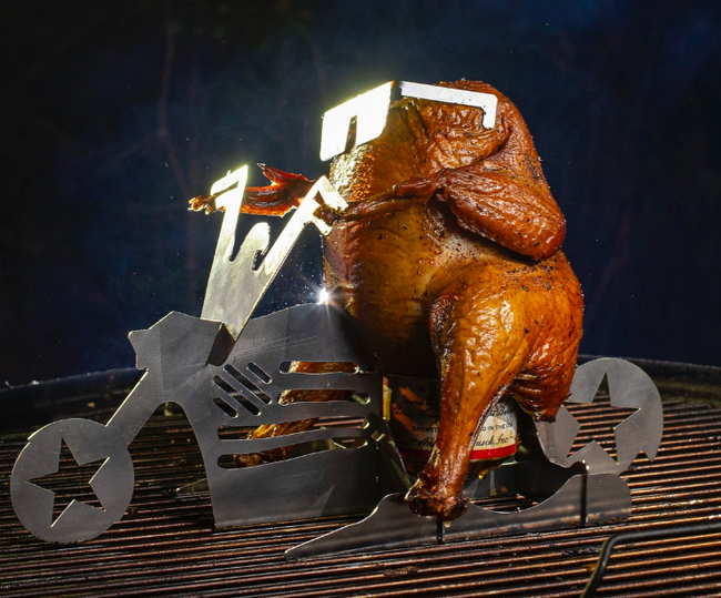 A roasted chicken cooking on a grill with a beer can chicken stand shaped like a motorcycle