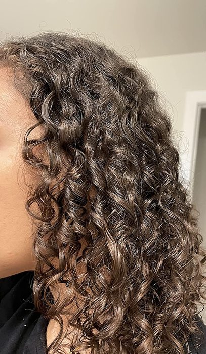 Close-up of a reviewer wearing a black top, displaying well-hydrated, tight brown curls after using the shampoo.