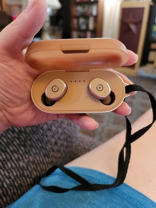 A reviewer holding a pair of golden wireless earbuds inside their case