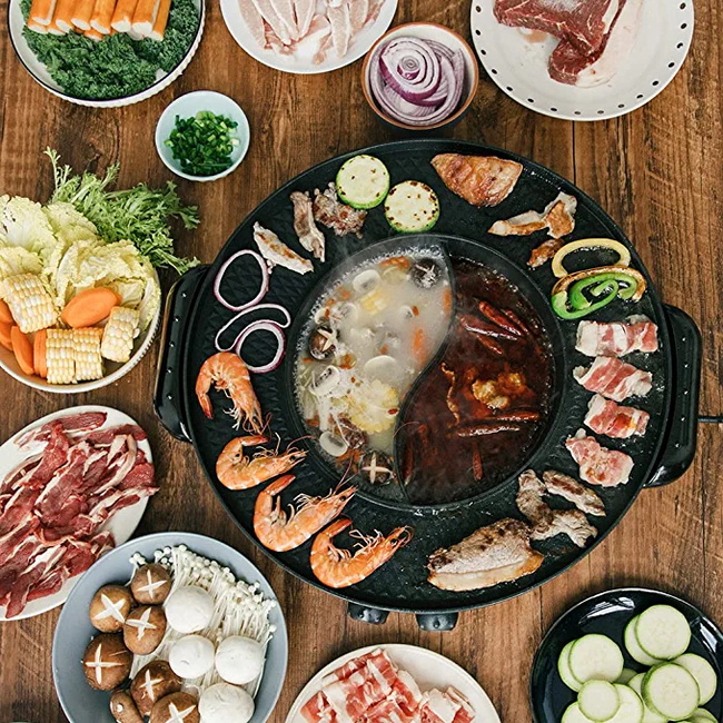 A hot pot and electric grill cooking shrimp, vegetables, and a variety of meats