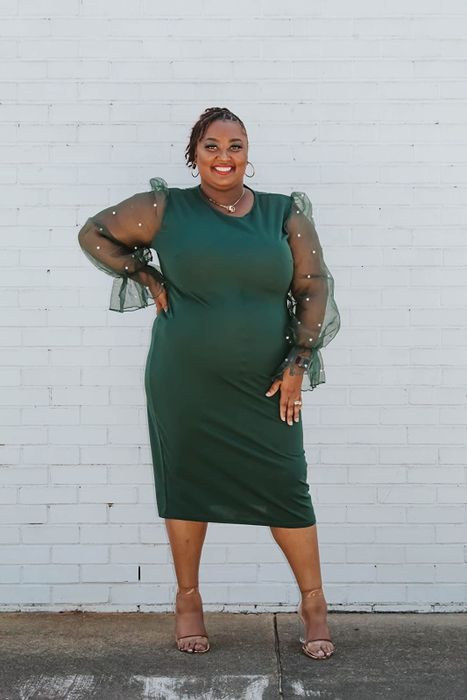 A reviewer dons a forest green pencil dress with long mesh sleeves embellished with pearls.