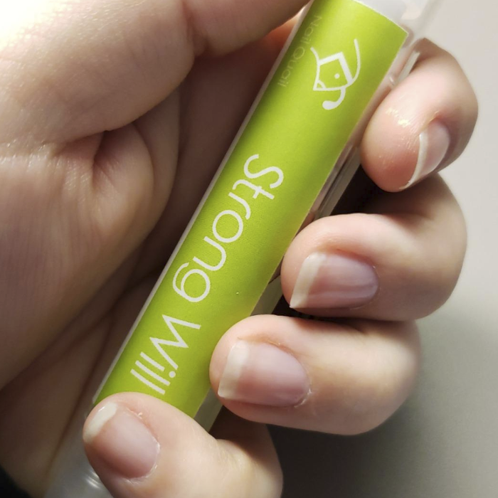 A reviewer's hand holding the anti-nail-biting pen, which features the words 