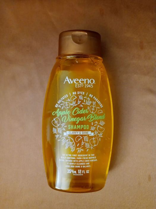 Image of a reviewer showing a clear bottle with yellow/orange shampoo against a brown backdrop.