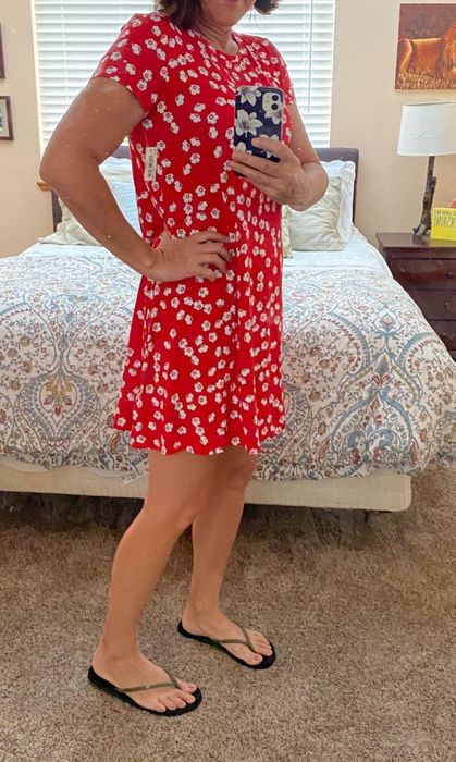 A reviewer is admiring herself in the mirror while wearing the red floral t-shirt dress