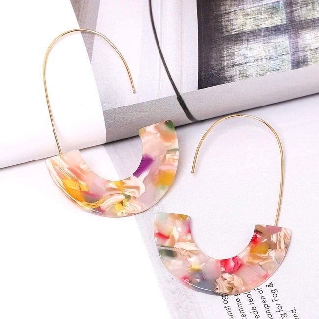 The earrings featuring gold wire hooks and half-moon multicolor resin hanging beneath them.