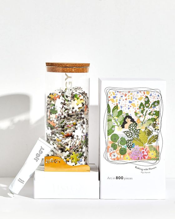 The puzzle box placed beside a glass container filled with the pieces, along with a tube of glue.
