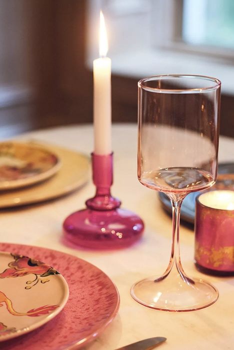 A pink wine glass placed on a table setting, with a candle flickering softly in the background.