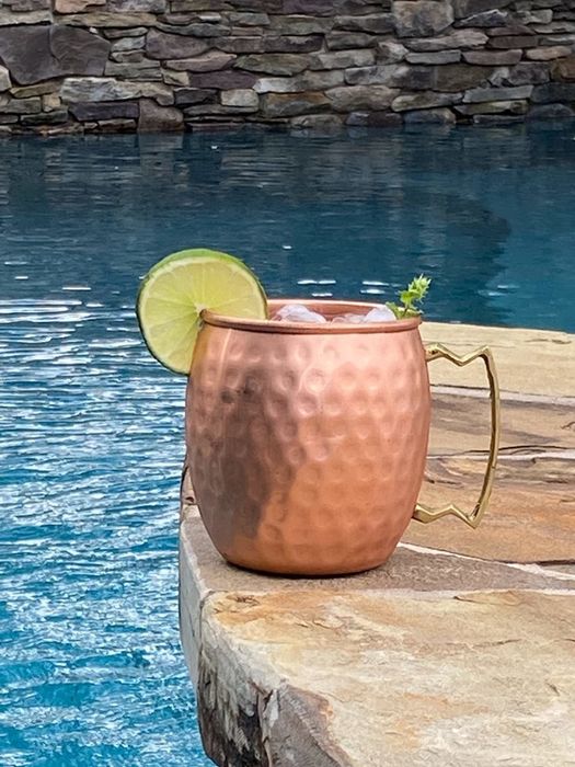 A reviewer image of the gold copper mug placed next to a pool.