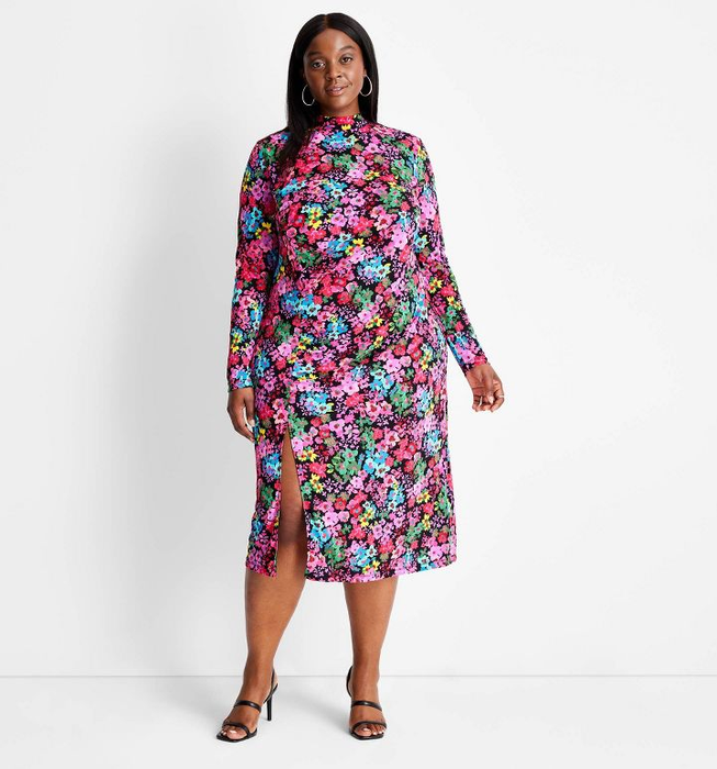 a model styled in a mock neck, long sleeve dress with a side slit and a vibrant multicolored floral pattern