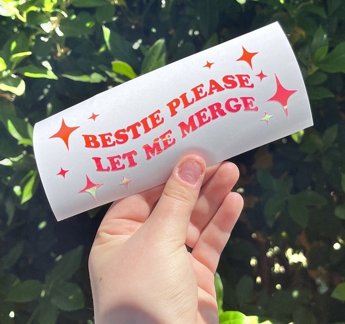 a hand holding the bumper sticker, which reads