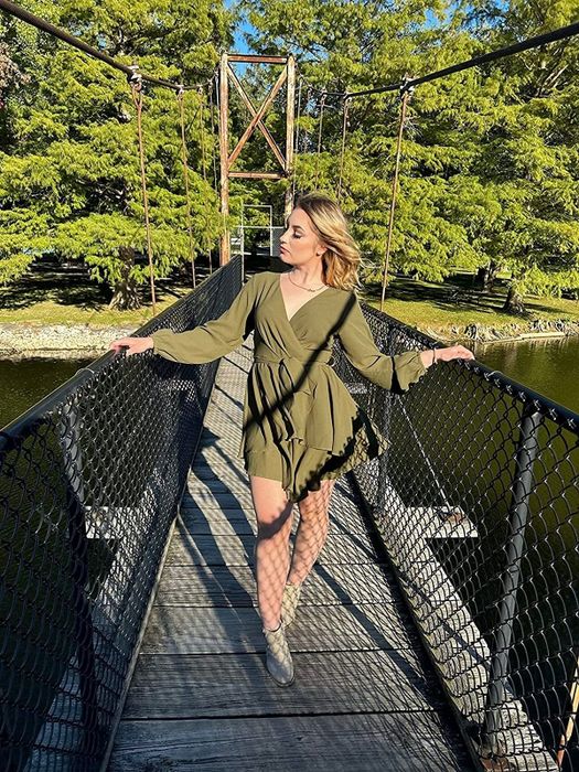 A reviewer wearing the dress in green, striking a pose on a bridge