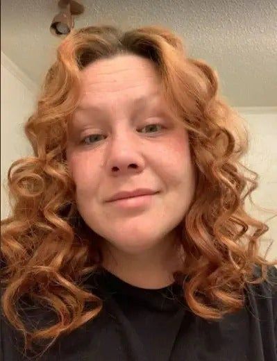 Reviewer showcasing their vibrant red, voluminous curls after using the product, dressed in a black top.
