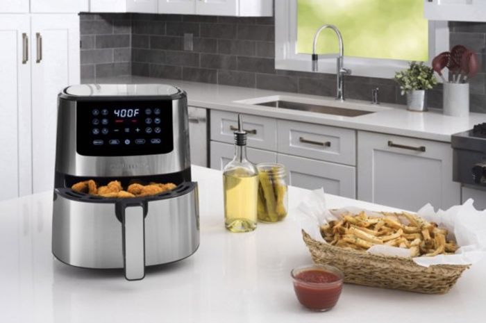 The air fryer with crispy breaded chicken nuggets alongside a basket of golden french fries on the counter