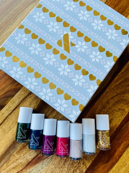 A blue box with six bottles of nail polish in colors including dark green, dark blue, maroon, pink, beige, light grey, and gold glitter.