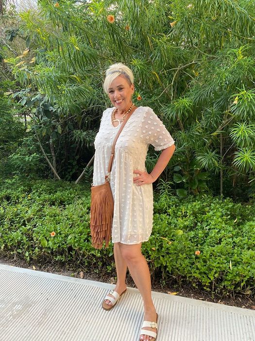 A reviewer in a white mini dress, accessorized with a brown bag