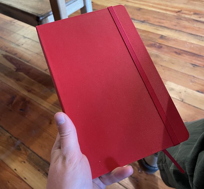 writer holding a red notebook with an elastic band
