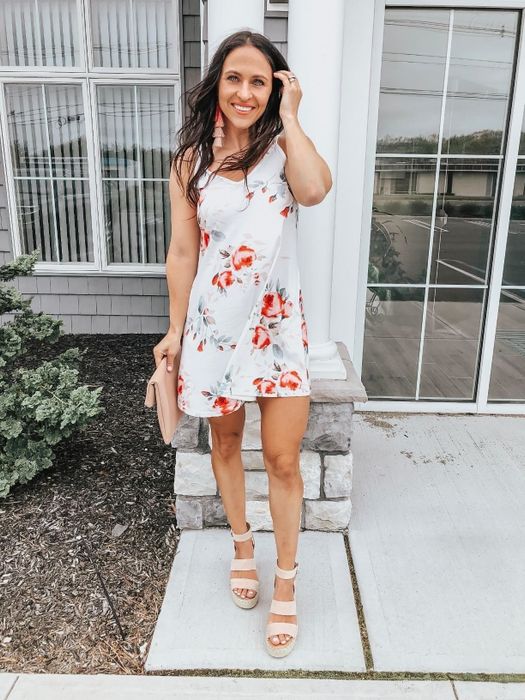 A reviewer wearing the white tank dress with a red floral print