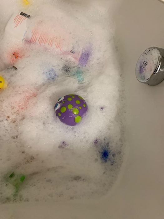 A reviewer's photo capturing a bubbly bath scene with children's toys floating in the water