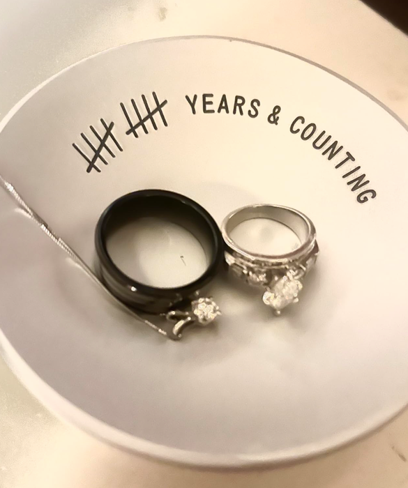 Two rings, one black and one silver, both adorned with diamonds, rest on a dish marked.