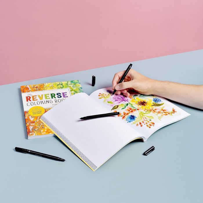 A model using a pen to outline around various abstract watercolor shapes inside the book