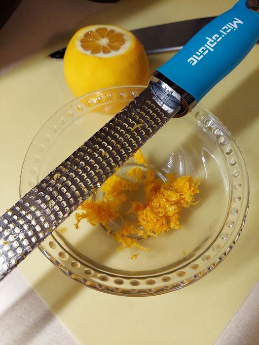 a microplane with a blue handle over a bowl of orange zest