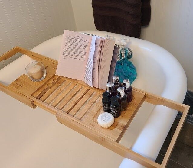 A reviewer’s photo showcasing the bamboo caddy resting on a bathtub, complete with a book and bath essentials arranged on it.