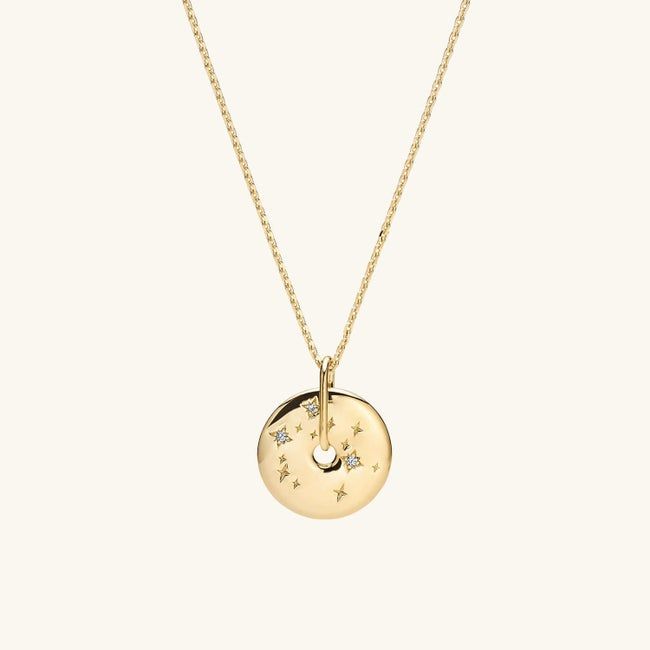The gold pendant shaped like a donut with a constellation pattern, hanging from a delicate chain.