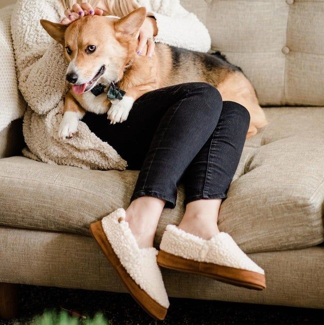 A model wearing slippers with brown soles and soft white shearling fabric on the top and sides.