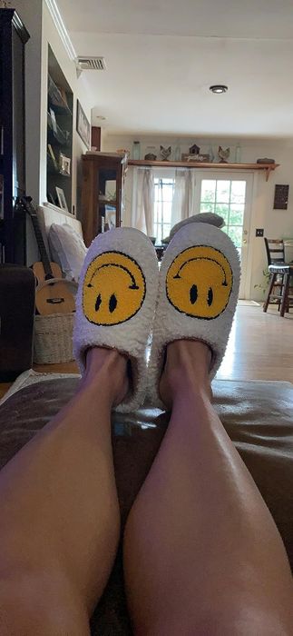 A reviewer wearing the white slippers with yellow smiley faces on them.