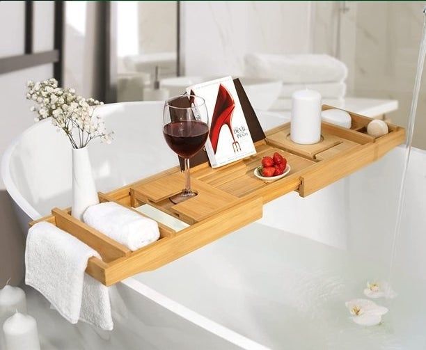 the bamboo bath tray with towels, a book, a glass of wine, strawberries, flowers, and a candle arranged on it