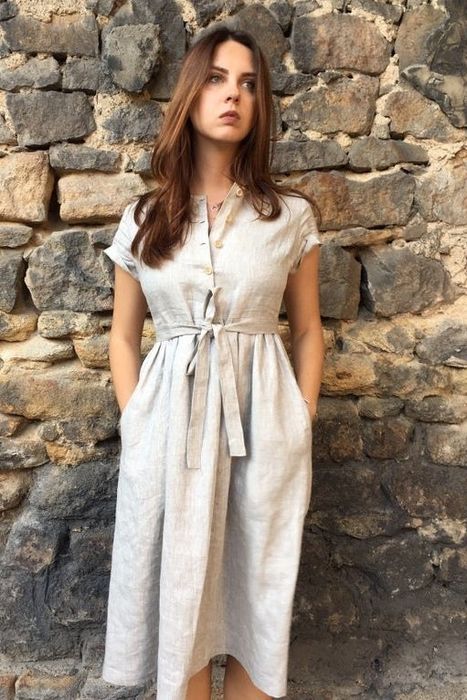 A model wearing a gray linen dress, hands tucked in the side pockets, and a sash tie belt cinched at the waist