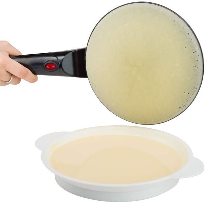 A hand holding the crepe maker by its handle after removing it from the batter bowl