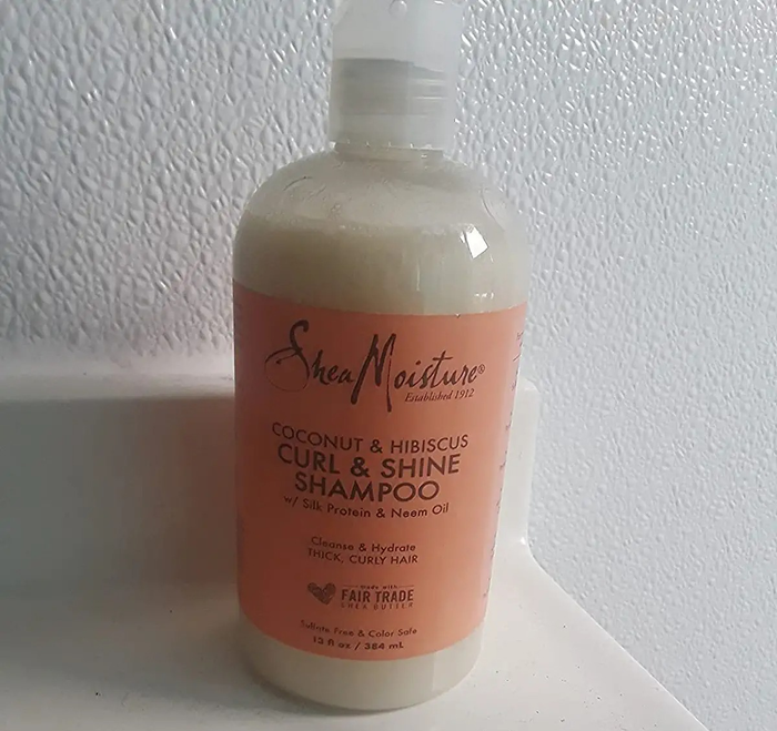 Reviewer image of a white and peach-colored curl shampoo bottle resting on a white countertop in front of a white wall.