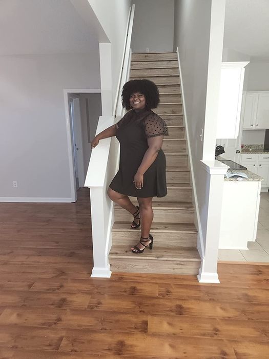 A reviewer poses in the little black dress with mesh sleeves on a staircase