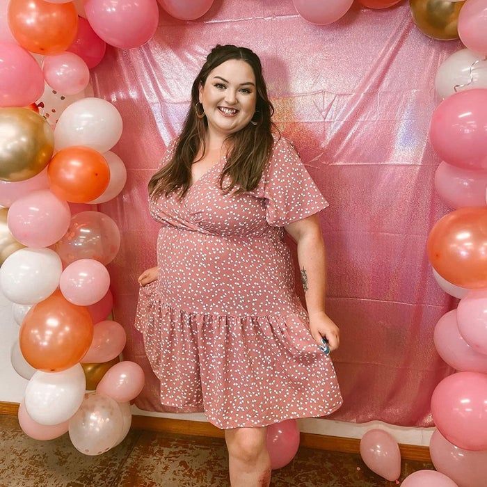 A reviewer showcasing the pink polka dot mini dress surrounded by colorful balloons