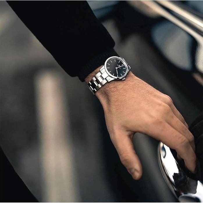 A close-up of a hand adorned with a stylish wristwatch featuring a metal band, reaching for a car door handle.