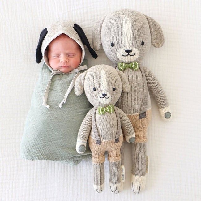 Two hand-knit dog plush dolls next to a newborn baby